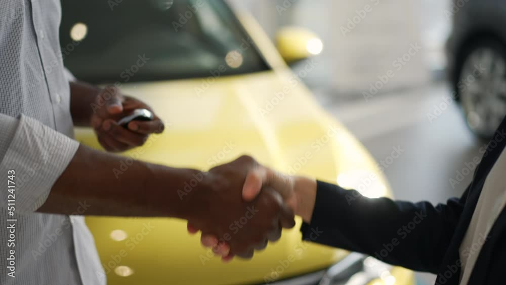 Male client is taking car keys from seller and shaking hands while standing in company spbas. 4k Close view of young American African man receives keys from agent and makes handshake, shows joy for