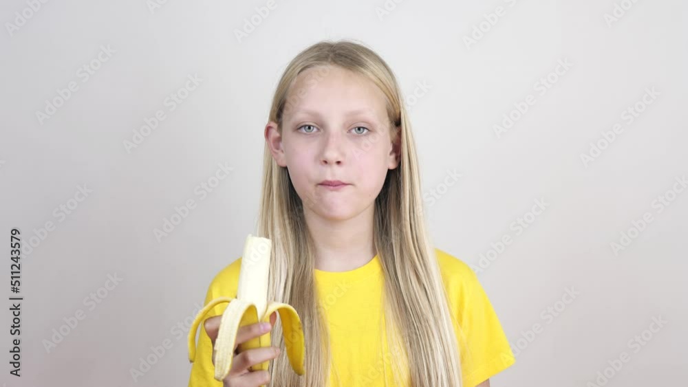portrait of a girl biting and eating a ripe banana, looking at the camera on a white background. Healthy food and beauty