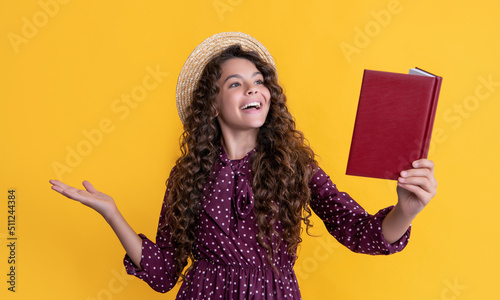 smiling child with frizz hair recite book on yellow background photo