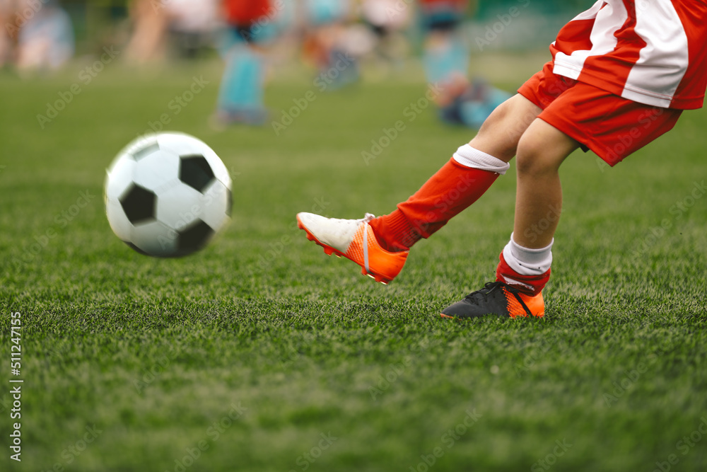 Soccer player kick ball on grass piitch. Football ball in motion. School soccer player in striped red and white uniform Soccer player kick ball on grass piitch. Football ball in motion. School soccer player in striped red and white uniform