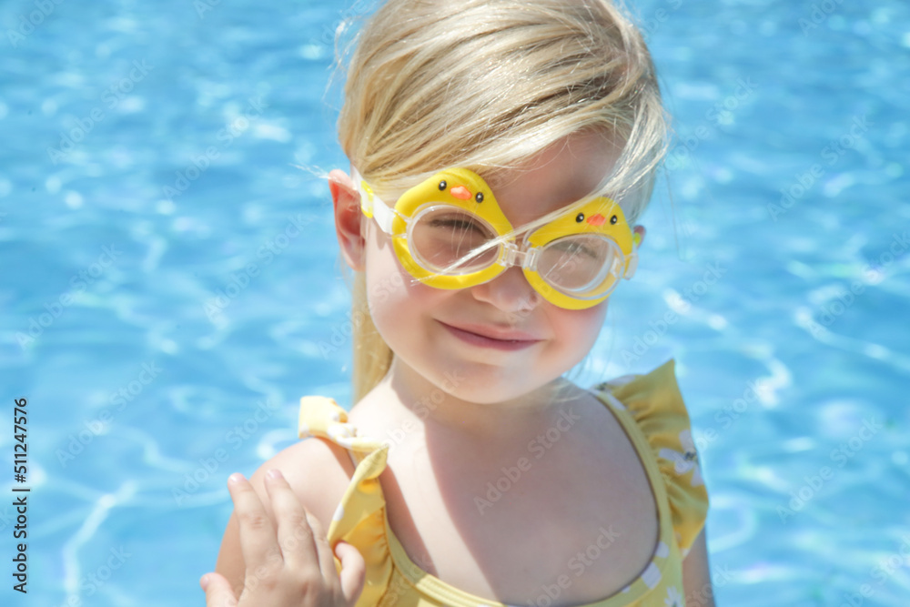 Portrait of toddler girl wearing swimming goggles with clear blue water background