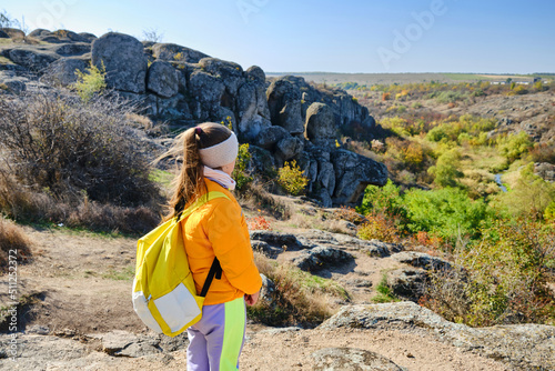 little girl with a backpack standing on a mountain top at the day time © Inna Vlasova