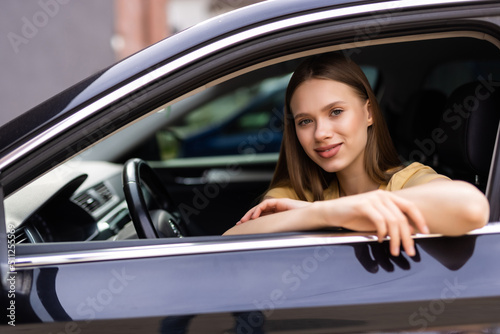 Happy smiling young woman or female driver driving car and drinking takeaway coffee