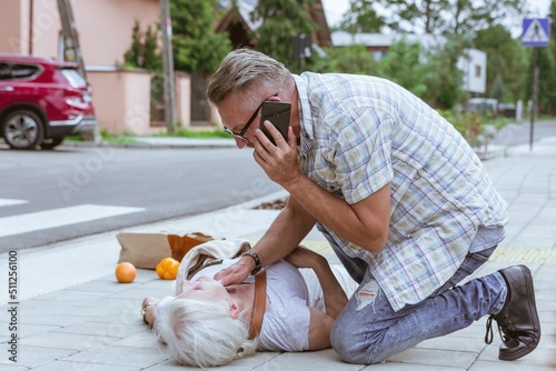 Senior passerby kneels beside the person who fainted on the street and calls an ambulance photo