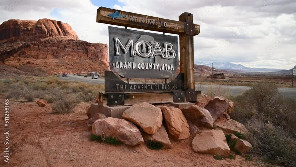 Welcome to Moab Utah sign on a cloudy day with vehicles driving on Highway 191, static