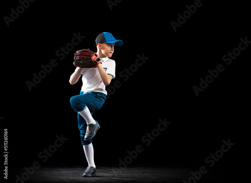 Canvas Print Dynamic portrait of little baseball player, pitcher in blue-white uniform training isolated on black studio background