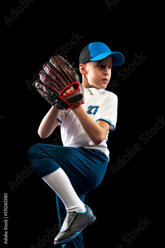 Canvas Print Dynamic portrait of little baseball player, pitcher in blue-white uniform training isolated on black studio background