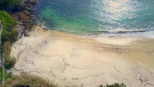 overhead drone image of the Galician coast of death in spain where we see the sea and the drone goes up and shows us the beach and the buildings during a sunny calm day with the small local buildings photo