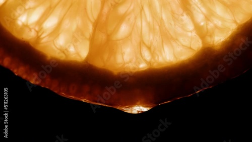 Juicy orange slice on black background. Citrus fruit close-up texture, healthy sweet food. Summer refreshment concept.