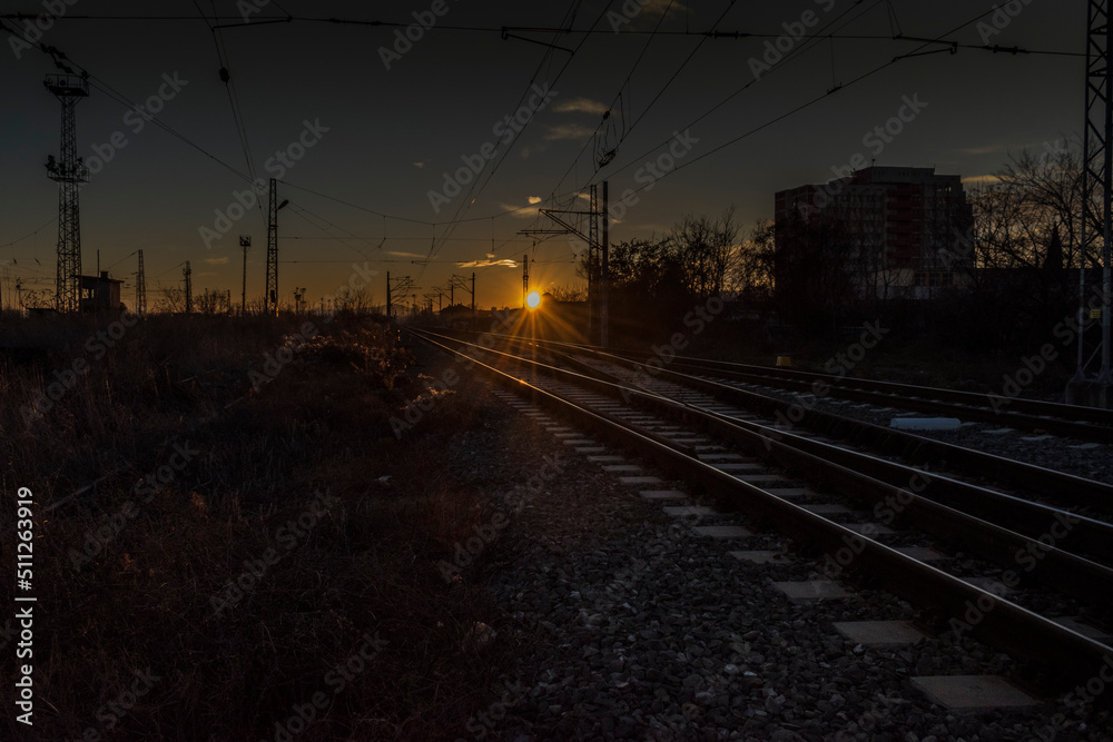 A scenic sunset over rail tracks near a station.