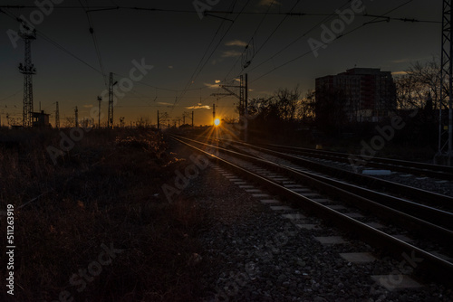 A scenic sunset over rail tracks near a station.