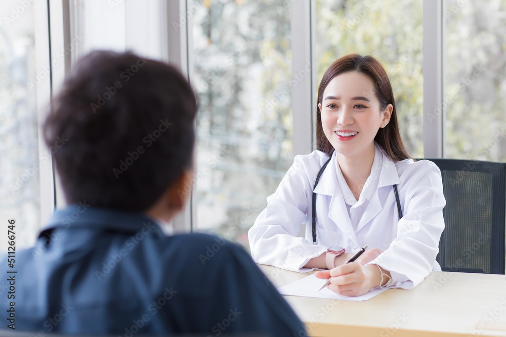 Obraz premium Asian professional woman doctor who wears medical coat talks with a man patient to consult and suggest healthcare information to him at the examination room in the hospital.