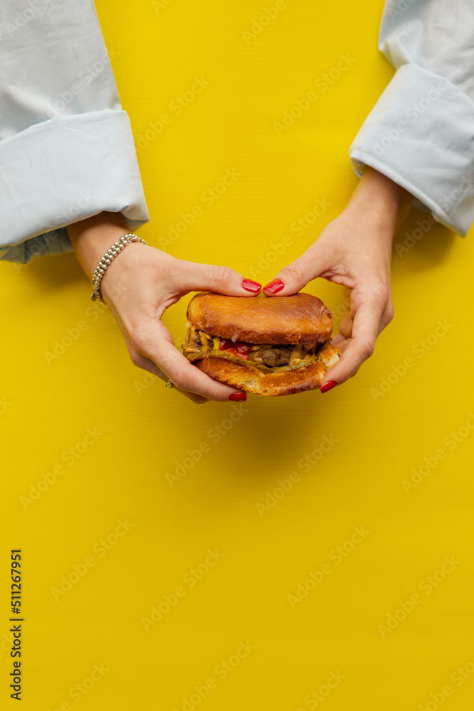 Classic cheeseburger in women’s hands on a bright yellow background. A succulent appetizing cheeseburger in the hands of both girls. Girl Holding Burger Two Hands Close Up