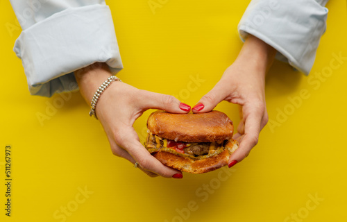 Classic cheeseburger in women’s hands on a bright yellow background. A succulent appetizing cheeseburger in the hands of both girls. Girl Holding Burger Two Hands Close Up