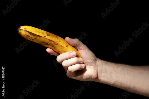 Man holds ripe banana in his hand like gun on black background photo