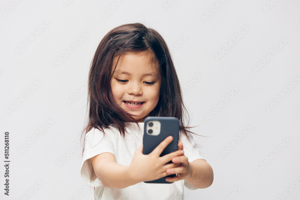 a funny, funny girl stands on a light background in a white T-shirt with her eyes closed and holds a new smartphone in her hands a funny, funny girl stands on a light background in a white T-shirt with her eyes closed and holds a new smartphone in her hands