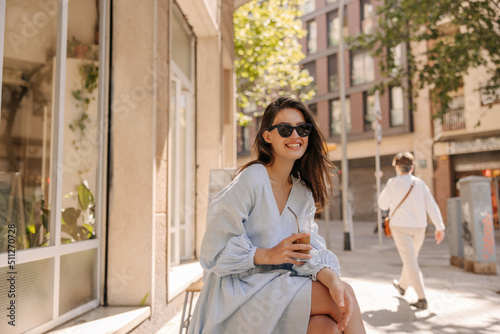 Murais de parede Happy young caucasian brunette woman in sunglasses drinking smoothie outdoors