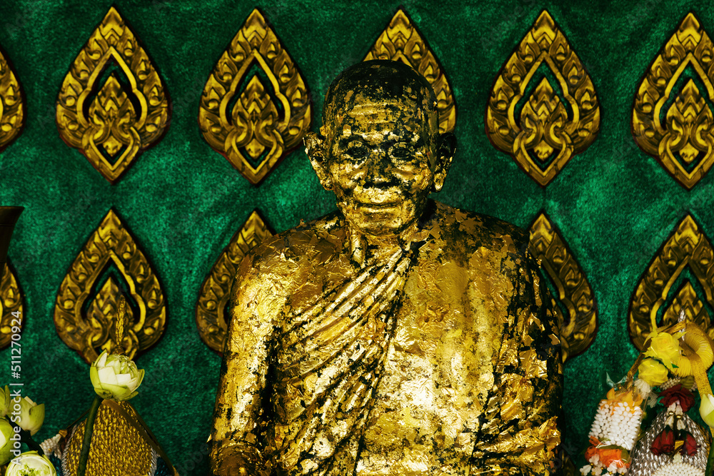 Closeup of praying buddhist monk covered in golden paint.