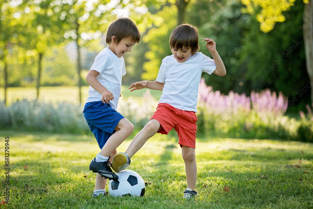 Two cute little kids, playing football together, summertime. Children playing soccer Two cute little kids, playing football together, summertime. Children playing soccer