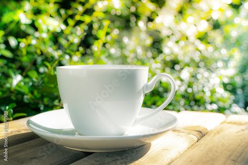 white ceramic coffee mug On the wooden floor, green tree bokeh background in the morning sun in the garden.