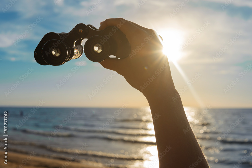 Adventure - Female hand with a vintage binocular against bright sun light on beautiful beach with nice blue sky.