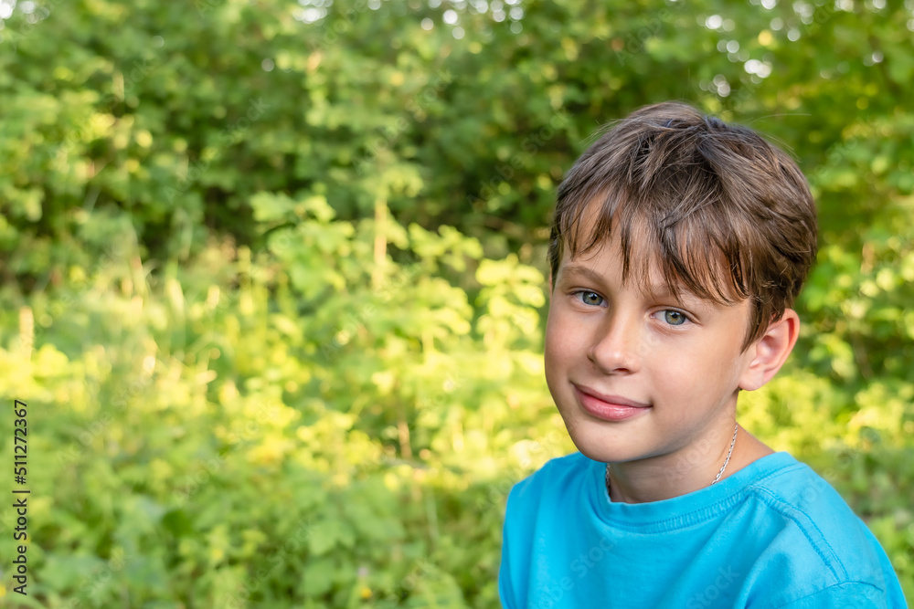 Smiling boy on a blurred background of trees. Portrait of a smiling 9 year old boy in a blue t-shirt in the garden Smiling boy on a blurred background of trees. Portrait of a smiling 9 year old boy in a blue t-shirt in the garden