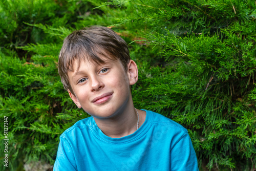 Portrait of a white caucasian 9 year old boy in a blue t-shirt. The child looks directly into the camera with a slight smile, tilting his head.