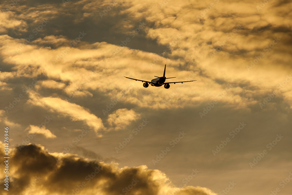 Fototapeta premium Silhouette of an airplane flying at sunset clouds.