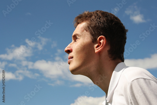 Young man face profile on a blue sky background. Photo was taken 15 June 2022 year, MSK time in Russia.