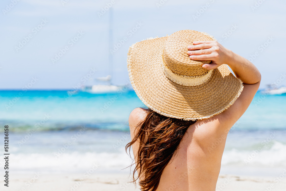 closeup of caucasian young girl sitting on the beach looking at the sea with straw hat