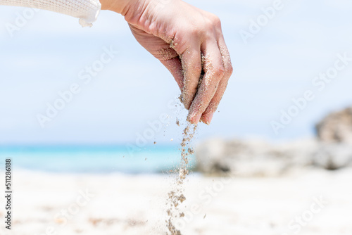 Hand of young woman releasing beach sand with the sea in the background