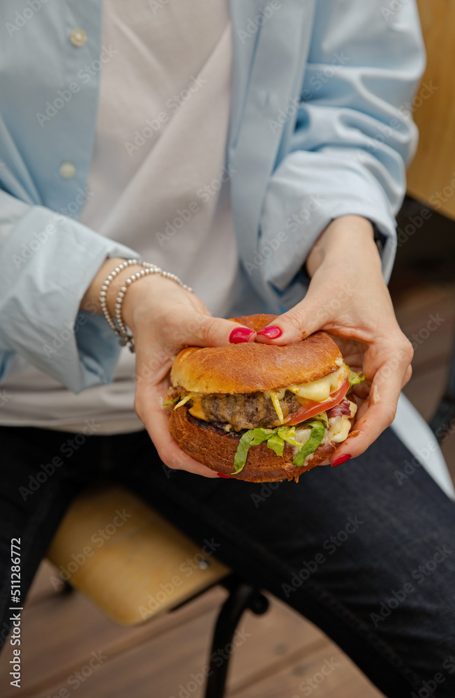 The girl is holding a juicy cheeseburger. A delicious burger in women’s hands close up. A perfect hearty dinner.