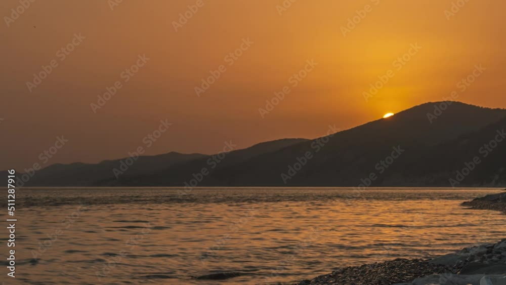 Timelapse beautiful sea sunset in black and yellow tones. Silhouettes of mountain hills on the background of water. The sun sets behind the mountain. Smooth camera approach. Sea evening landscape Timelapse beautiful sea sunset in black and yellow tones. Silhouettes of mountain hills on the background of water. The sun sets behind the mountain. Smooth camera approach. Sea evening landscape