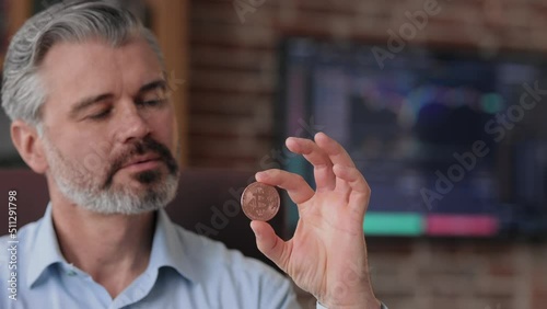 Portrait of businessman holding bitkoin in office interior with stock market graphs on background. Using bitcoins as payment. Investitions in cryptocurrency. Buying and selling using bitcoin. photo