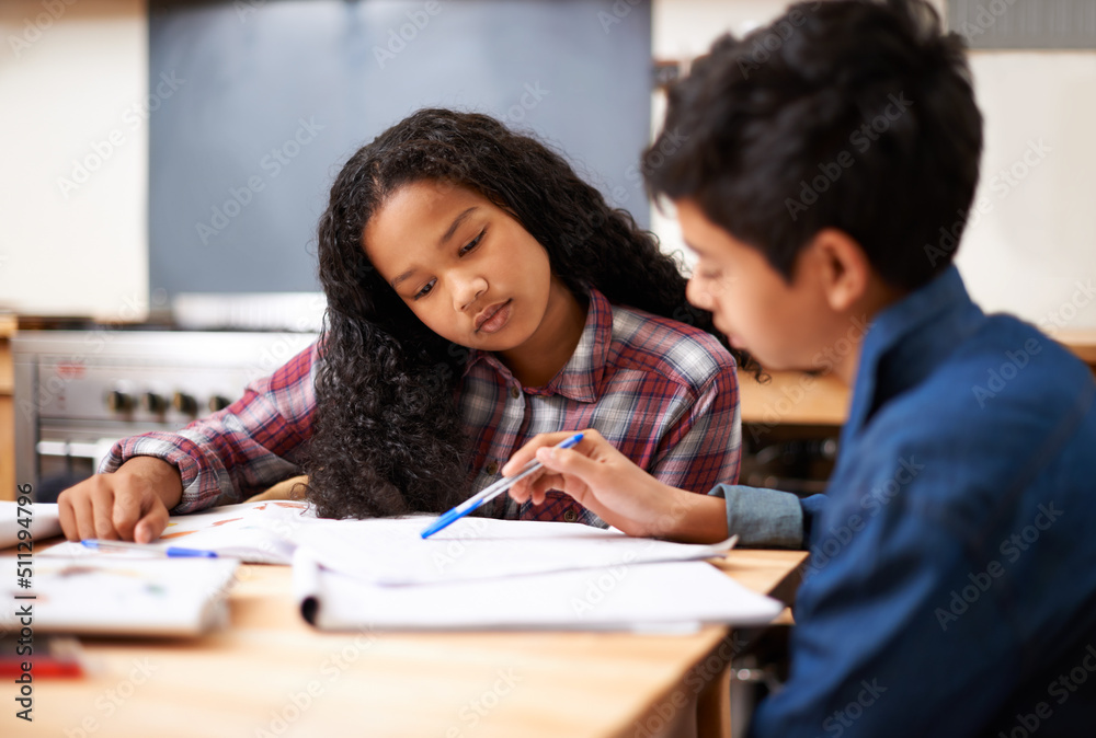 Solving their homework together. Shot of two young students studying together in a classroom.