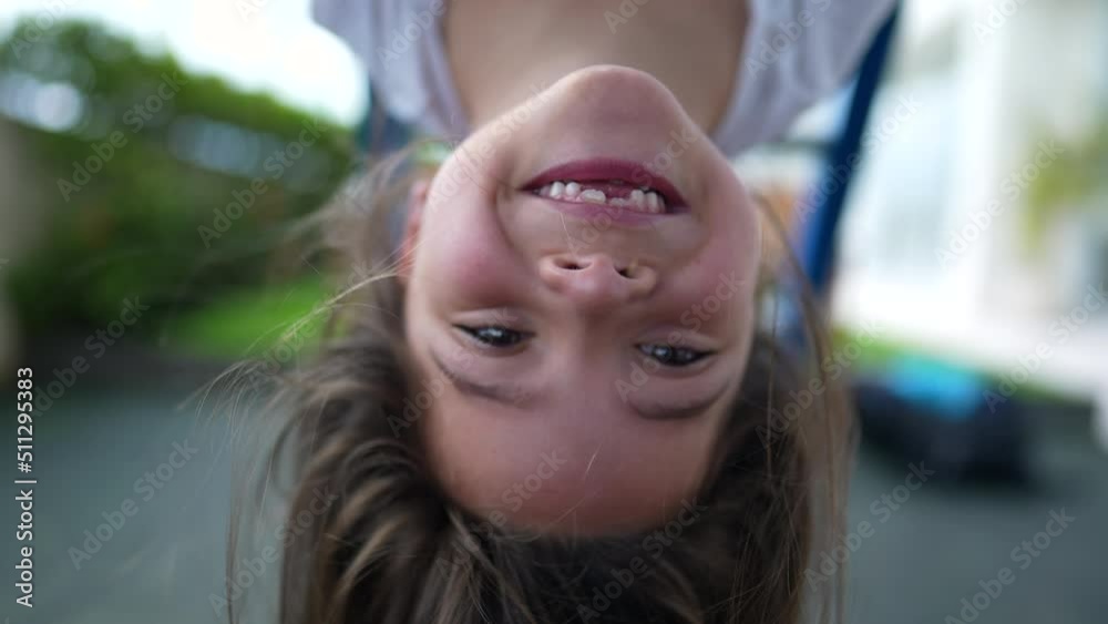 Carefree little girl hanging upside down at playground child plays at monkey bar enjoying summertime