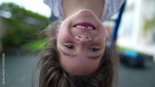Carefree little girl hanging upside down at playground child plays at monkey bar enjoying summertime photo