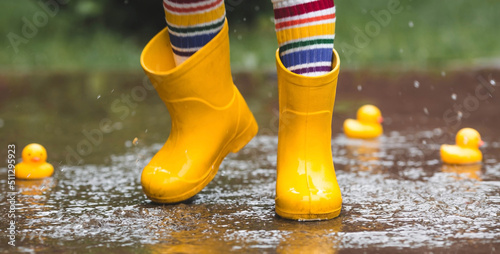 Obraz na płótnie A small child in rainbow-colored socks and yellow rubber boots jumps through puddles and plays with yellow rubber ducks