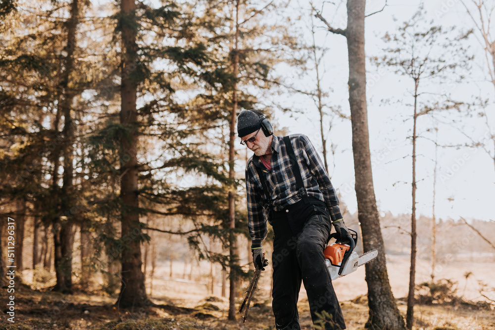 Senior man in forest holding chainsaw Senior man in forest holding chainsaw