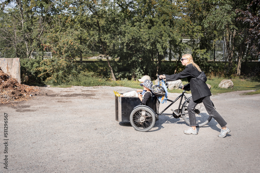 Mother pushing bicycle with children in carriage Mother pushing bicycle with children in carriage