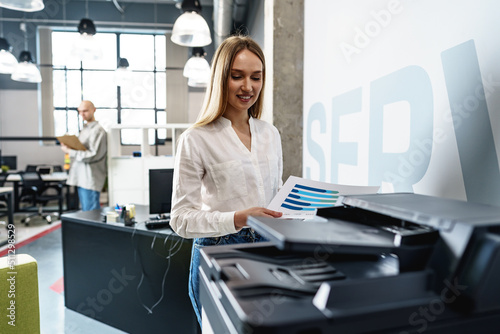 Young employee using modern printer in office photo