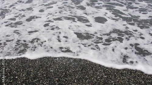 Sea tide on a pebble shore. Waves with white foam on a pebble beach. Nature concept, vacation, background