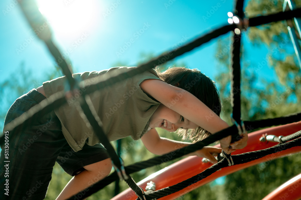 Fototapeta premium A child climbs up an alpine grid in a park on a playground on a hot summer day. children's playground in a public park, entertainment and recreation for children, mountaineering training.
