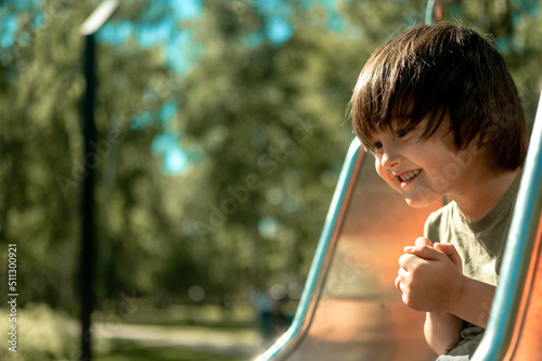a boy in the park on a playground is rolling down a slide. A child walks on a hot sunny day. the concept of a happy childhood. Asian-looking kid with long black hair laughs