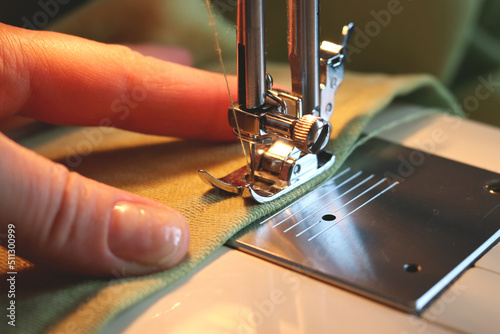 A seamstress sews clothes from green fabric on a sewing machine. Lowered needle and thread close-up of the thread. Selective focus