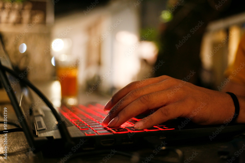 Person typing on a keyboard. Close up of young man working late night with laptop in the cafe