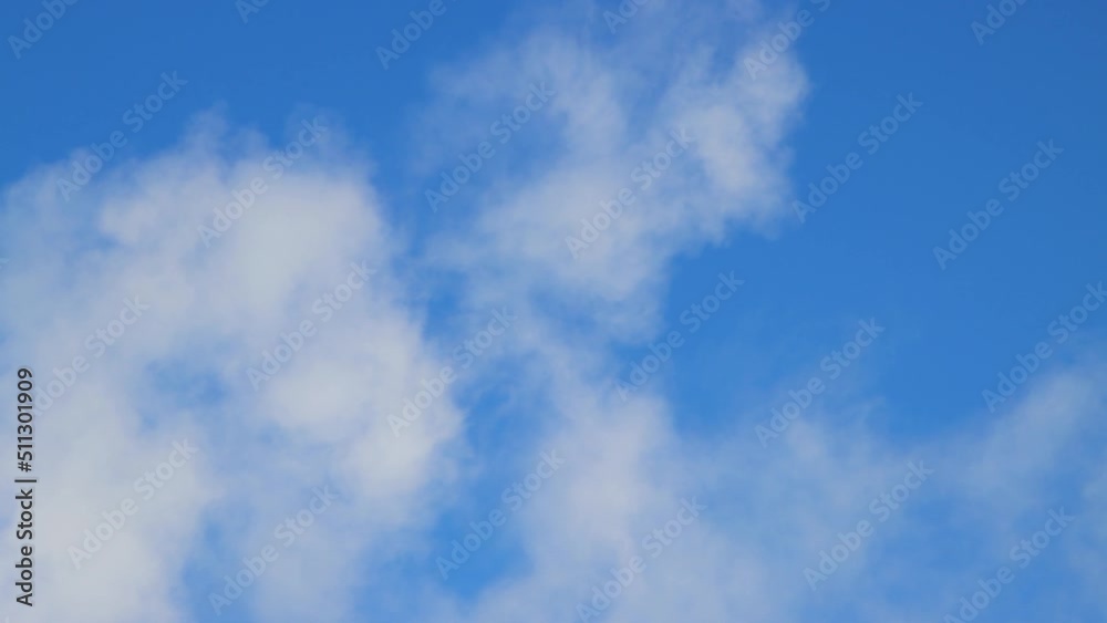 A white fluffy cloud moves against the blue sky. Summer or winter time lapse, clear sky, warm light, panorama. Video, screensaver background, for titles, intro, transition. UHD 4K.