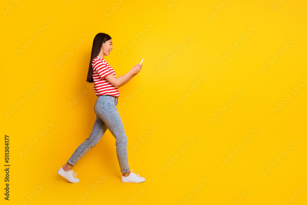 Full body profile photo of amazed excited girl walking use telephone typing isolated on yellow color background Full body profile photo of amazed excited girl walking use telephone typing isolated on yellow color background