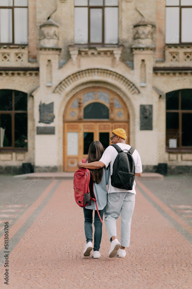 International students couple walking to the university building hugging each other, wearing stylish clothes