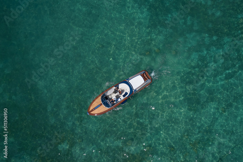 Classic Italian wooden boat aerial view. Man and woman on an expensive wooden boat top view. Top view of a wooden powerful motor boat. Luxurious wooden boat on transparent turquoise water, top view.